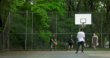 Group of friends playing basketball on outdoor court surrounded by trees, teamwork and competition creating energy and camaraderie in relaxed urban park environment - Powered by Adobe