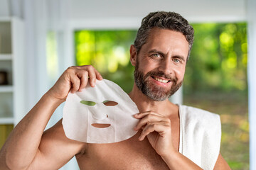 Hispanic male use moisturizing facial beauty mask. Collagen for glowing skin. Man with cloth...