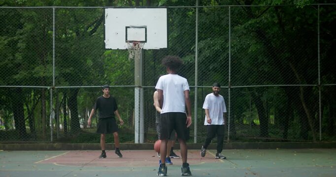 Group of friends playing basketball on outdoor urban court, enjoying teamwork and competition surrounded by trees, expressing energy, friendship, and connection through sport - Powered by Adobe