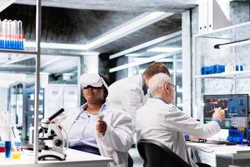 Fototapeta premium Black woman using VR headset to explore 3D interactive experiment in laboratory, biochemistry and nanotechnology study. Expert uses virtual reality glasses and gadgets for science.