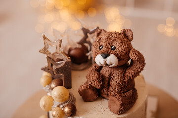 Close-up of fondant teddy bear on birthday cake decorated with stars and golden balls.