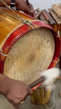 Vertical Close-Up: Musician's Hands Playing Traditional Tambora Drum with Mallet, Creating Rhythmic Folk Music