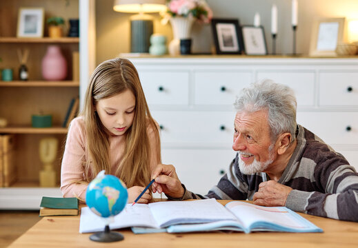grandfather  teaching granddaughter and helping her with homework at home