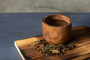 tea drink in a wooden cup and dry tea leaves on a wooden cutting board.