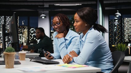 Black women working together with data insights on desktop in workspace, developing business...