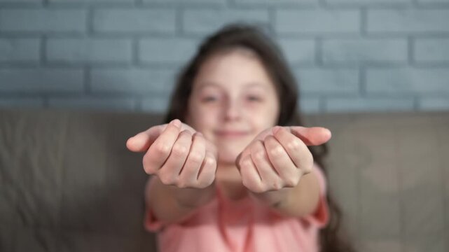 Joyful child ask for hugs. A view of joyful little girl with extending hands sitting on sofa indoor
