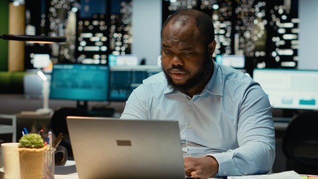 African american guy at the workspace sitting in deep concentration, pondering for a decision. Using laptop as he applies rational thinking and intuition for issue, mental haze. - Powered by Adobe