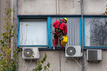 Man worker hanging on a facade building with protective equipment washing windows outside