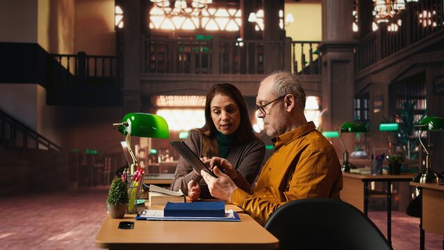 Focused students taking notes from academic library resources and reviewing archived materials in a study area, showing the dedication of mature education and knowledge building.