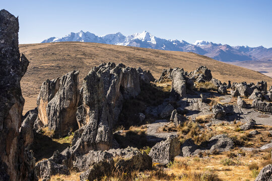 Striking view of the Hatun Machay stone forest in Ancash, Peru. Massive, eroded rock formations stand in a high-altitude Andean landscape, with the snow-capped Cordillera Blanca in the distance.