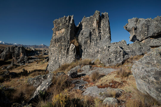 Striking view of the Hatun Machay stone forest in Ancash, Peru. Massive, eroded rock formations stand in a high-altitude Andean landscape, with the snow-capped Cordillera Blanca in the distance.