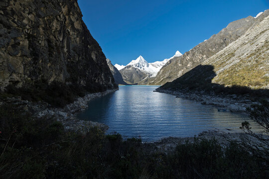 Breathtaking view of  Paron lake, a stunning turquoise glacial lake in Peru's Cordillera Blanca, near Caraz. Steep cliffs frame the water, leading to snow-capped peaks under a clear blue sky.