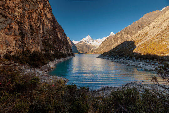 Breathtaking view of  Paron lake, a stunning turquoise glacial lake in Peru's Cordillera Blanca, near Caraz. Steep cliffs frame the water, leading to snow-capped peaks under a clear blue sky.
