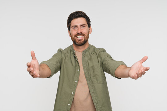 Overjoyed happy man standing with his hands wide open. Laughing male model posing at studio photoshoot want to hug person. Image of kind cheerful guy isolated on white background. Invitation concept