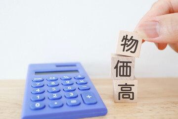 物価高をイメージした木のブロックと青い電卓。コピースペースあり。