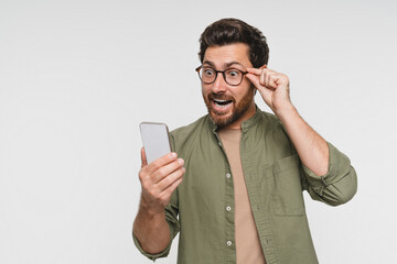 Head shot portrait shocked man looks at screen open mouth make big eyes holds phone astonished by received sms feels stunned surprised amazed pose studio white wall, unbelievable news concept