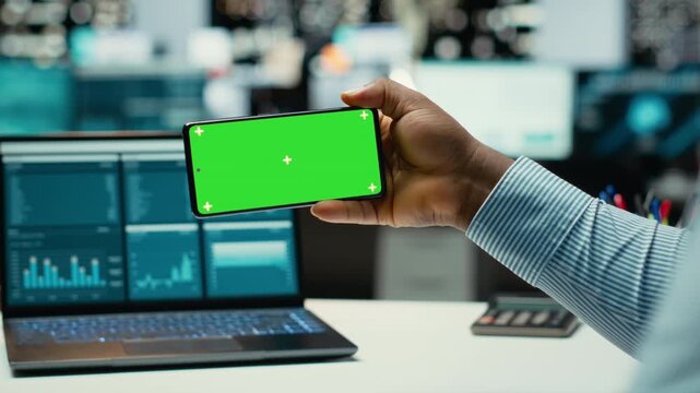 African american man working with green screen on mobile phone in modern space, checking online insights in strategy room. Male general manager handling business administration. Camera B.