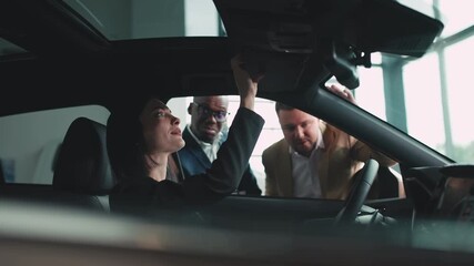 Woman sitting in a car at a dealership, smiling while discussing options with a salesman, showcasing the car buying experience in a modern showroom environment