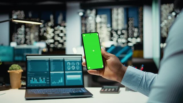 Black male consultant in office uses green screen on smartphone after hours, scheduling new meetings and planning the weekly agenda. Business management tasks for a company project. Camera A.