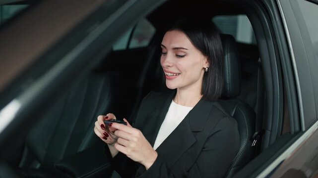 Smiling woman in black blazer holding car key inside vehicle, showcasing excitement of new car purchase, representing the joy of buying a car