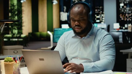 African american guy handles daily tasks late at night with ambience music on headset, finding inspiration with focus sounds to help with concentration and productivity. Male multitasking. Camera B. - Powered by Adobe