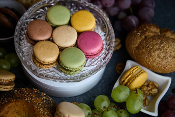 Macaron stack in small bowl with grapes and bread rolls rustic tabletop