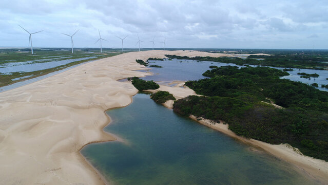 Vista panor&acirc;mica dos Pequenos Len&ccedil;&oacute;is Maranhenses em Paulino Neves, com dunas douradas, lagoas de &aacute;gua cristalina e torres e&oacute;licas sob o c&eacute;u azul do Maranh&atilde;o