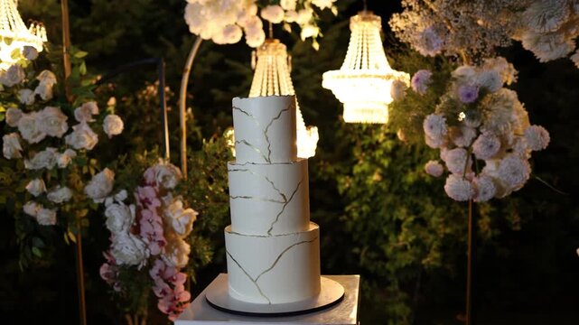 White wedding cake standing on a table outside with flower decorations