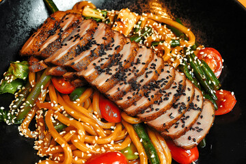 Sliced grilled duck breast served on a bed of noodles with fresh vegetables and sesame seeds