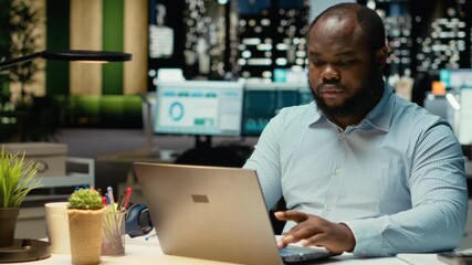 African american weary man struggling to stay awake after hours in office, trying hard to work and finish task. Person feeling overworked and overwhelmed after hours, sleep deprivation. Camera B.