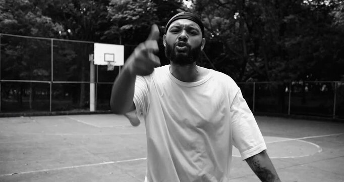 African American man wearing durag confronting camera with intense stare on outdoor basketball court, dramatic monochrome POV confrontation scene