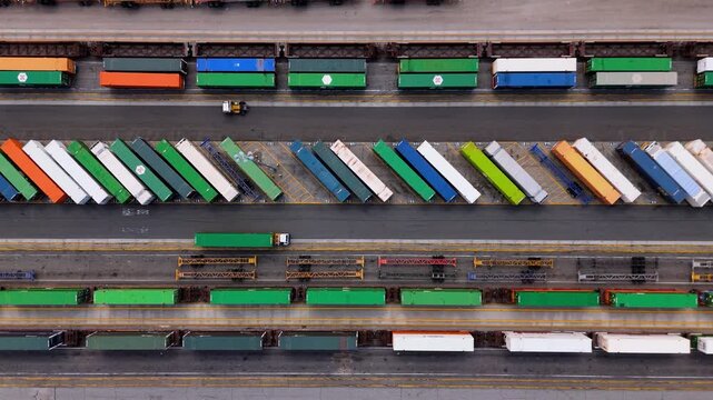 Aerial view of cargo truck moving between colorful containers and train platforms, October 7, 2025