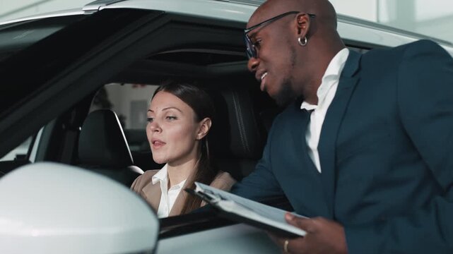 A smiling woman discusses car options with a man, demonstrating the buying process and customer service in a modern showroom.