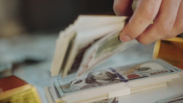 Close-up of male hands counting a thick stack of hundred-dollar bills over a table covered in cash and gold bars, representing wealth, corruption, investment, and financial success