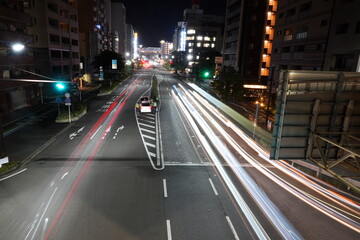 Obraz premium 夜の交差点を見下ろす高所からの長時間露光撮影で自動車のヘッドライトやテールランプの光跡が鮮やかに写り込んでいる都会の夜景です。建物の窓の光も印象的です。