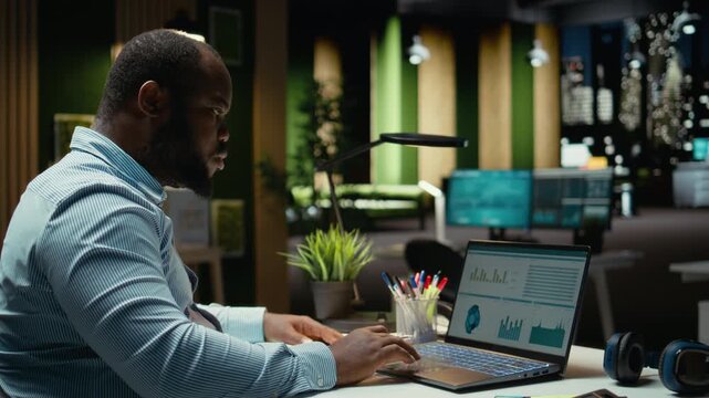 Black business consultant working late at night on proofreading documents, writing reports on laptop. Creating a summary and designing strategy to align with company objectives. Camera A.