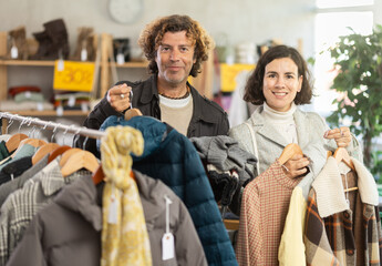 Married couple stands in the interior of a store and chooses outerwear on sale. Husband and wife shopping at the mall on discount days