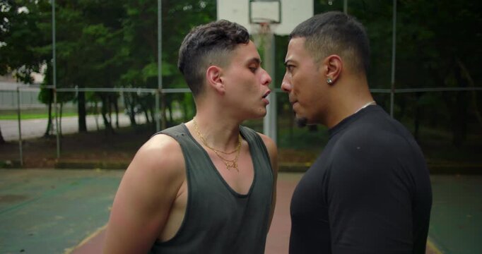 Two Hispanic men face off in intense standoff during street basketball game, heated argument and confrontation escalating on outdoor court under rising tension