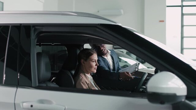 A female buyer and male salesperson discuss vehicle specifications in a dealership showroom, demonstrating customer interaction and the buying experience in the modern automotive environment.