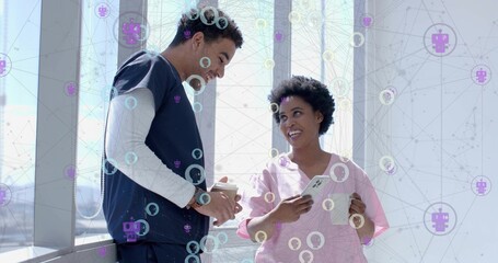 Standing medical staff wearing scrubs talking in hospital corridor, with smartphone and coffee cup © vectorfusionart