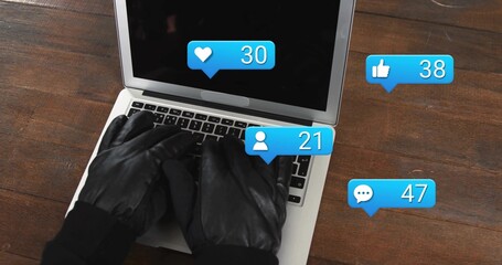 Typing gloved hands using silver laptop keyboard on dark wooden desk, with social media alerts