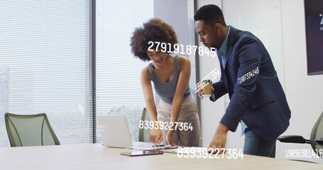 Leaning over table, business professionals analyzing numeric data on laptop in conference room