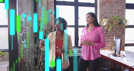 Collaborating women in blazers holding marker, analyzing stock charts on glass board in loft office