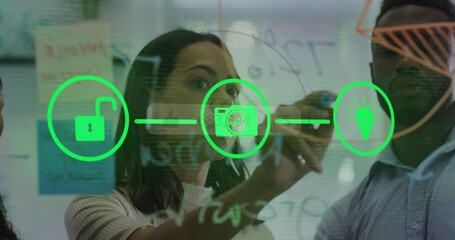 Woman in ribbed sweater sketching neon green icons on glass board in office, with sticky notes