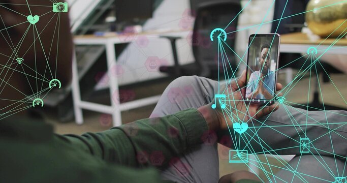 Man wearing green shirt holding smartphone showing live feed in office with globe and digital icons