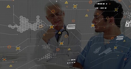 Doctor in coat consulting nurse in scrubs in hospital hallway reviewing data with tablet overlays