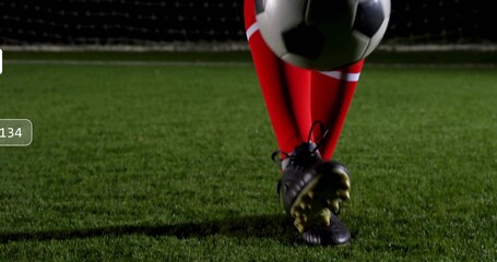 Balancing soccer player wearing black cleats controlling ball on green turf at night, with goal net