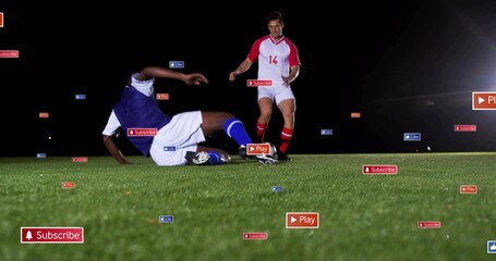 Sliding soccer player in blue kit tackling red opponent on turf under lights, with floating icons