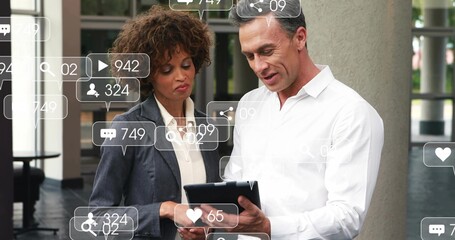 Two business professionals analyzing tablet at corporate entrance, with digital overlay icons