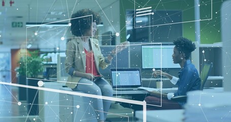 Two coworkers in casual wear discussing network overlay at office desk with laptops and tablet